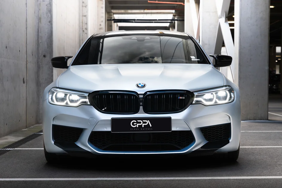 Бяло BMW M5 отпред в бетонен паркинг