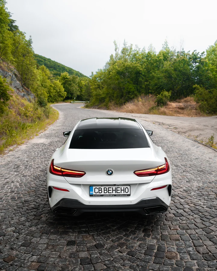 Бяло BMW купе отзад на планински път с калдъръм